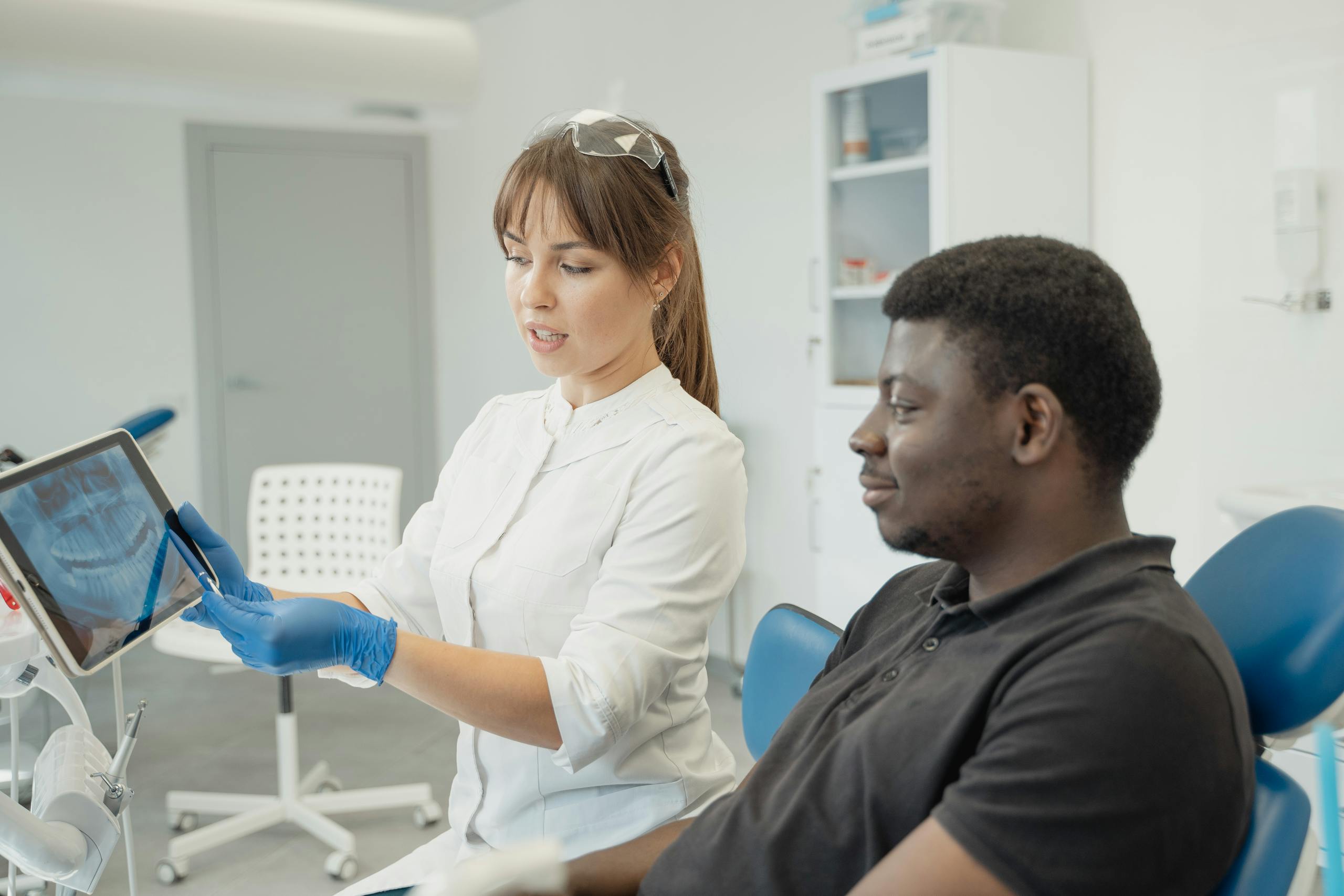 A dentist explains dental x-ray results to a patient using a digital tablet in a modern clinic setting.